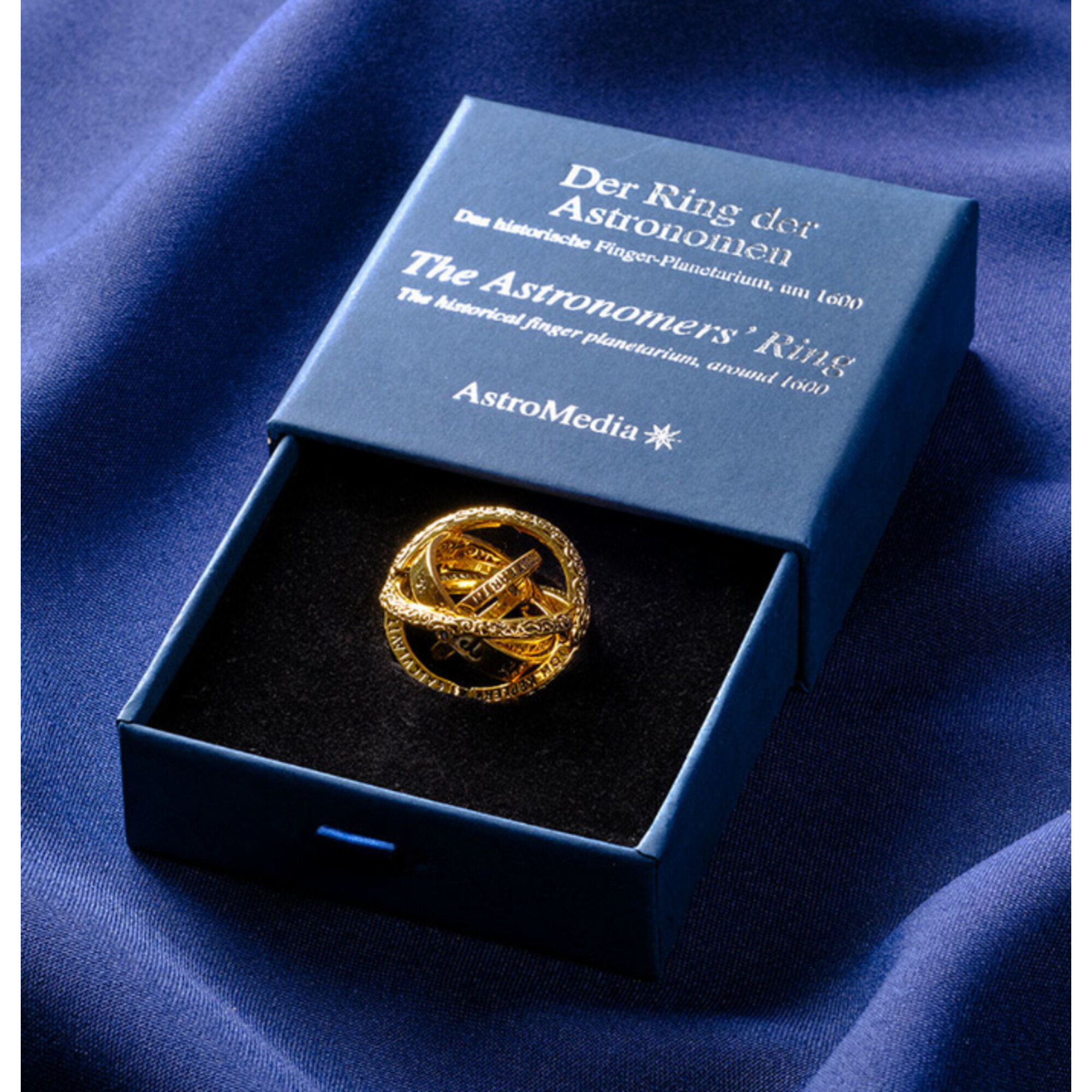 Goldener astronomischer Ring im blauen Karton auf blauem Stoff.
