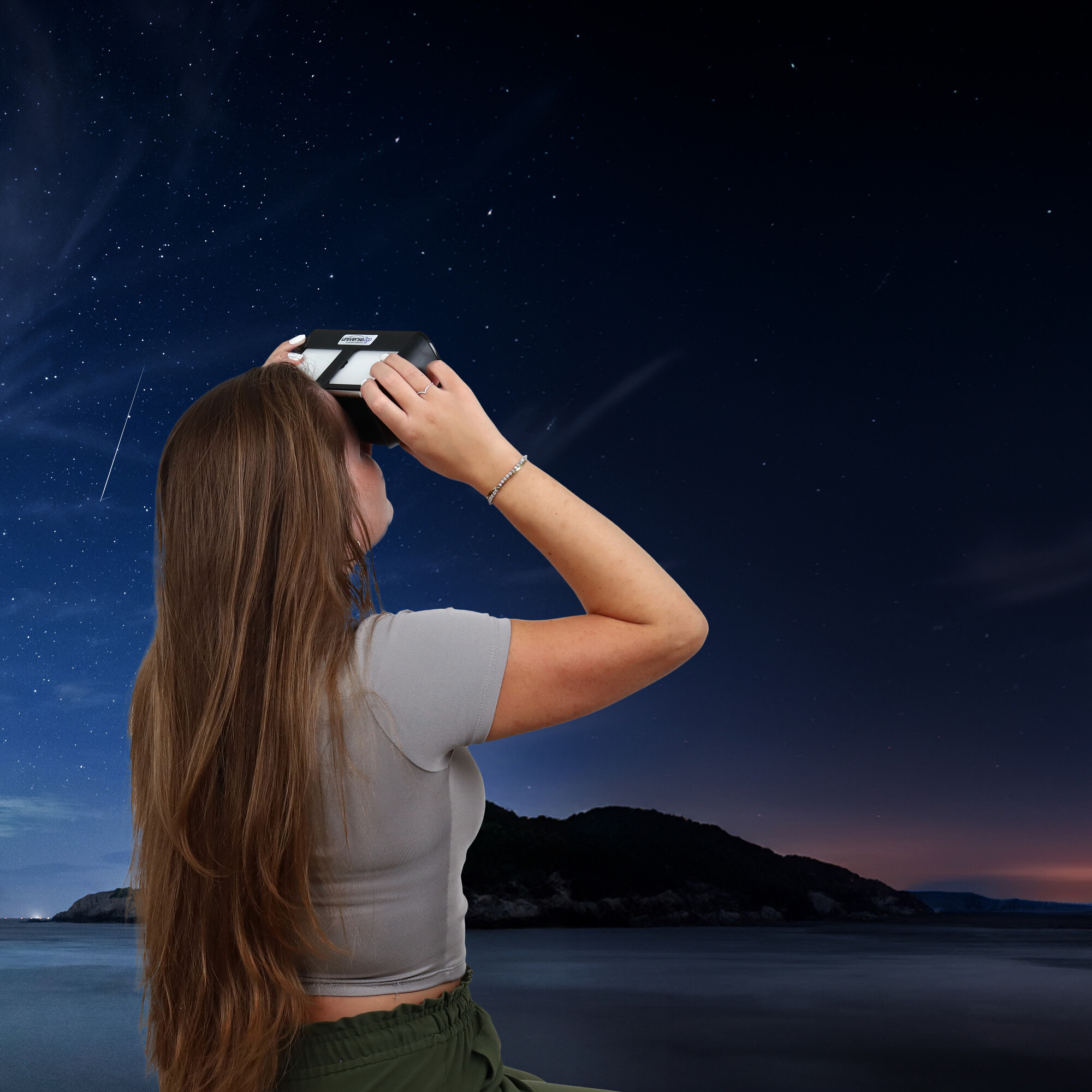 Frau blickt durch Fernglas in sternenklaren Nachthimmel über dem Meer.