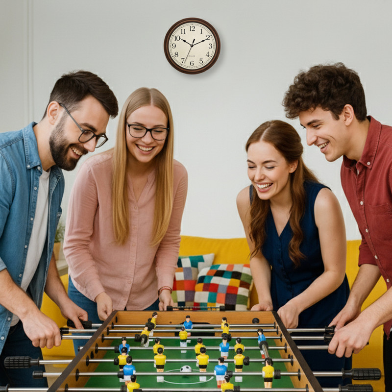Vier Freunde spielen Tischfußball und lachen. Eine Wanduhr hängt an der Wand.