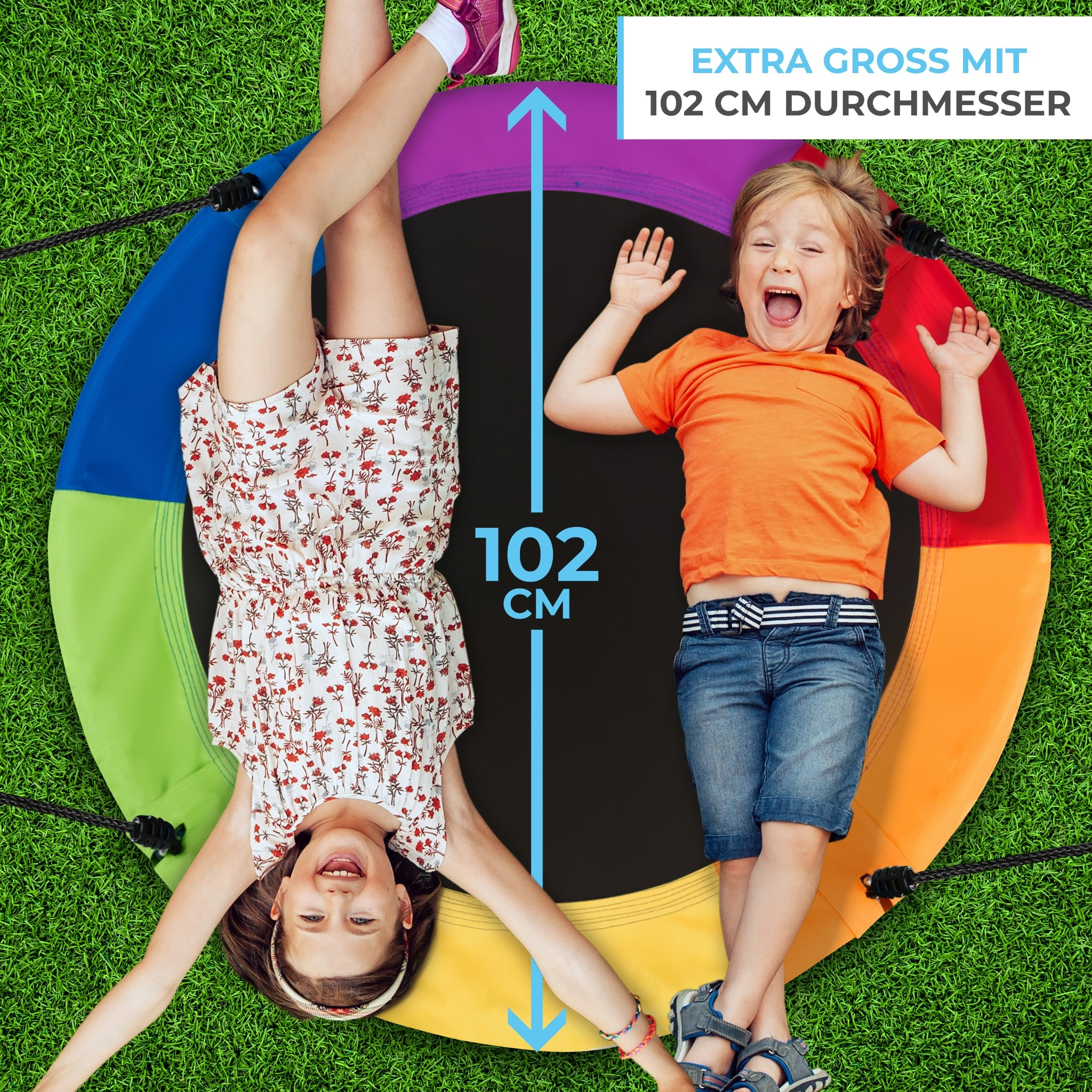 Zwei Kinder liegen auf einer bunten 102 cm großen Schaukel über grünem Gras.