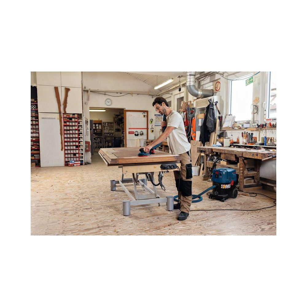 Mann schleift Holz in Werkstatt mit Staubsauger und Werkzeugen.