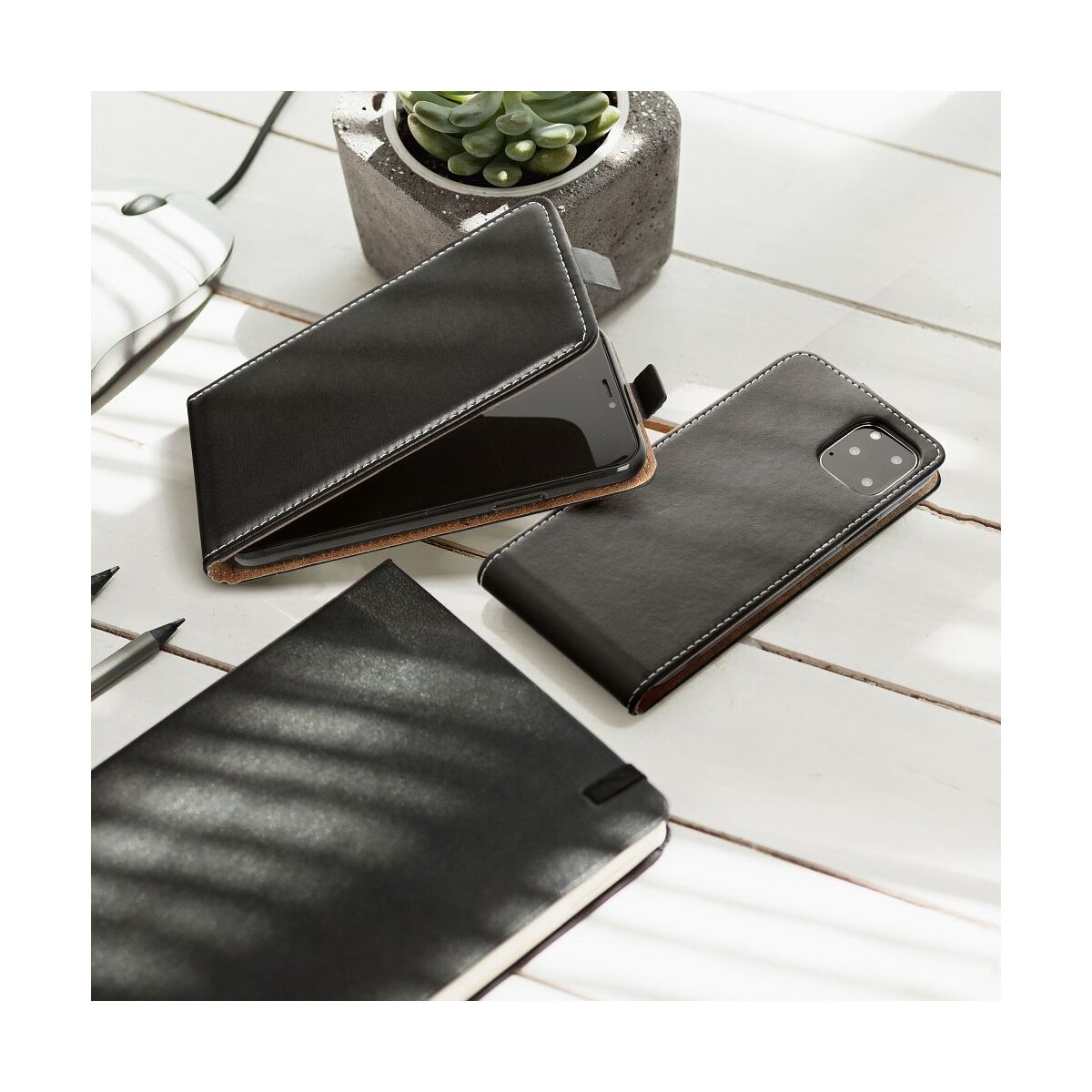 Schwarzes Leder-Handycover, Notizbuch, Maus und Pflanze auf weißem Holztisch.