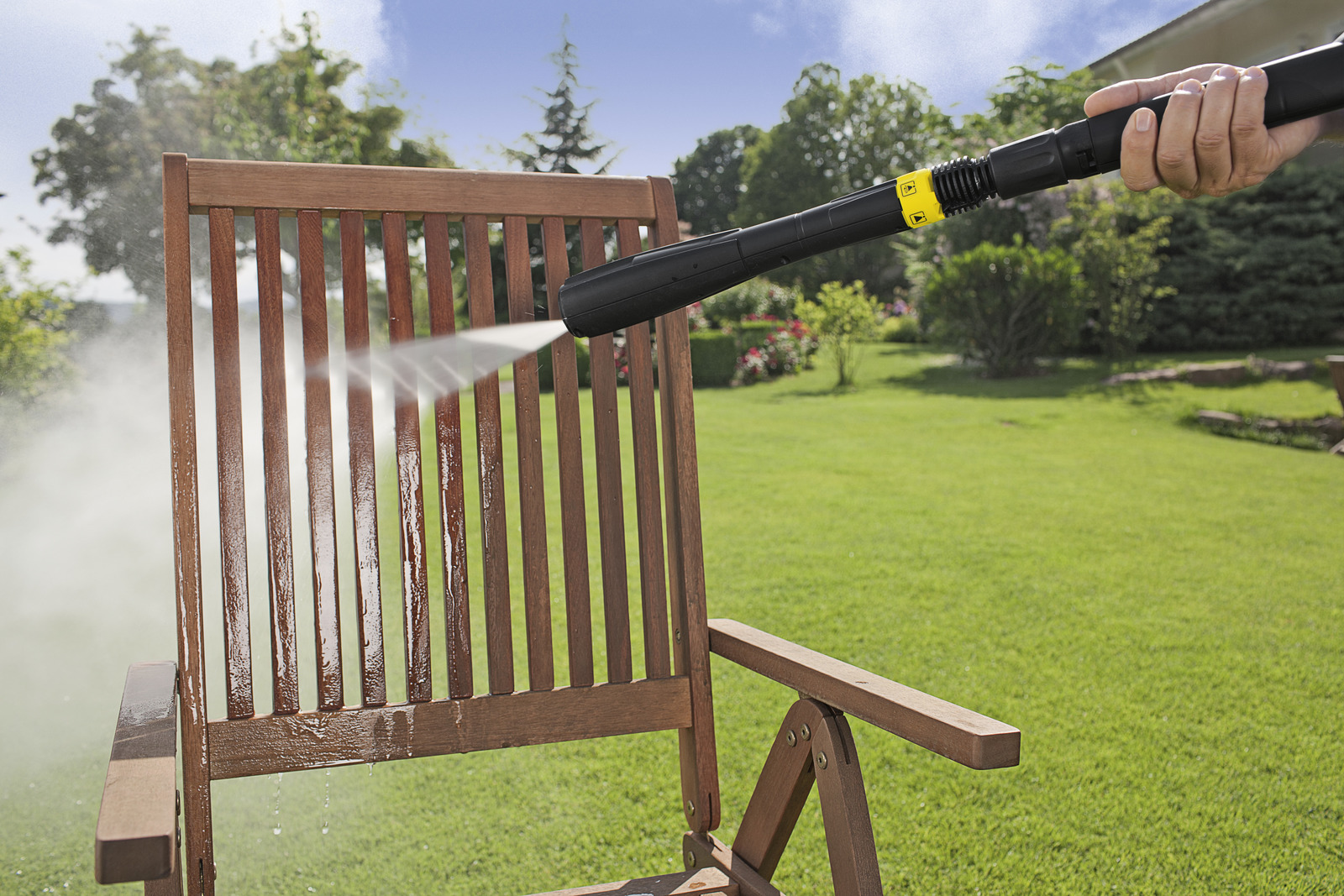 Una sedia di legno viene pulita in giardino con un'idropulitrice.