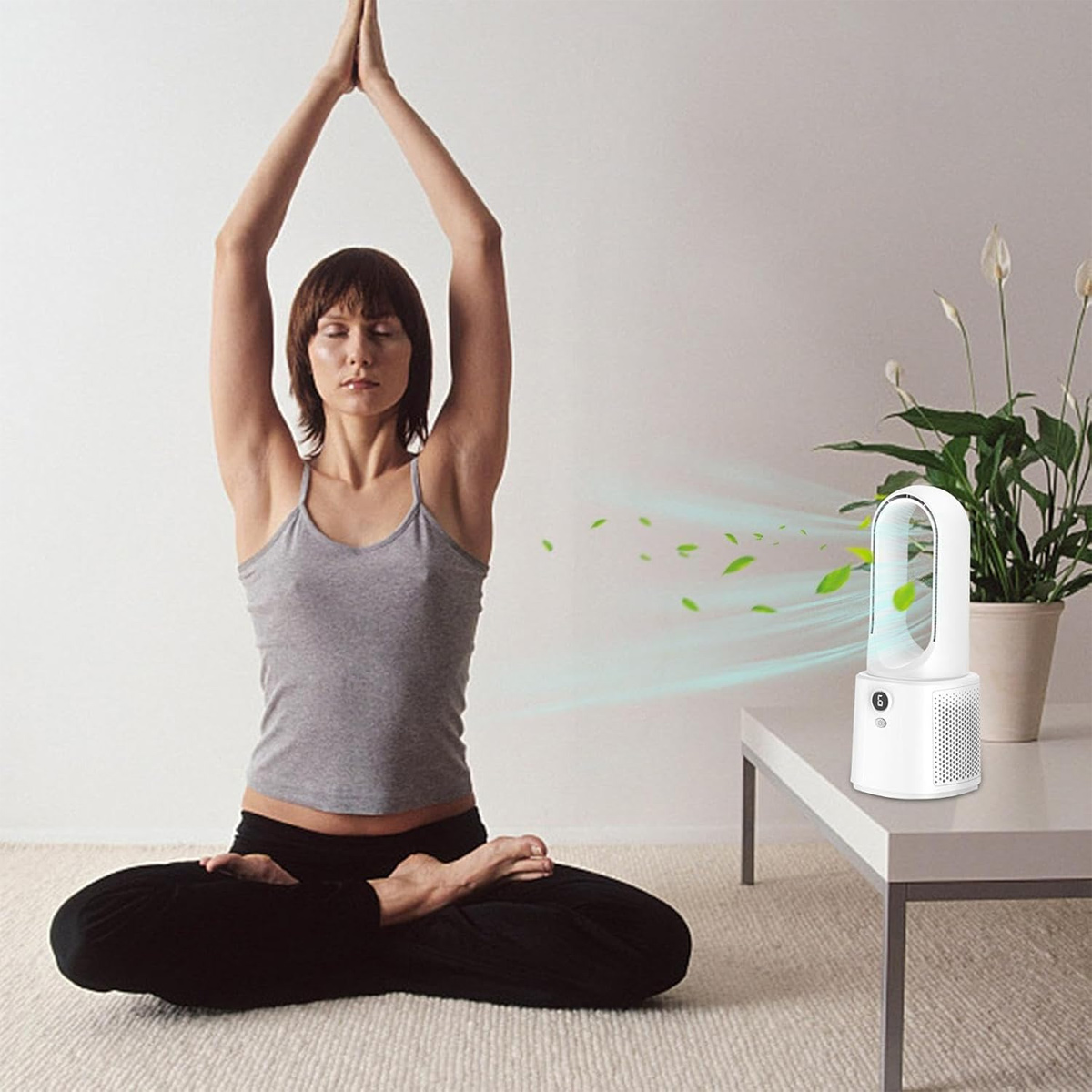 Frau in Yoga-Pose neben einem weißen Ventilator, der Luft und Blätter bläst.
