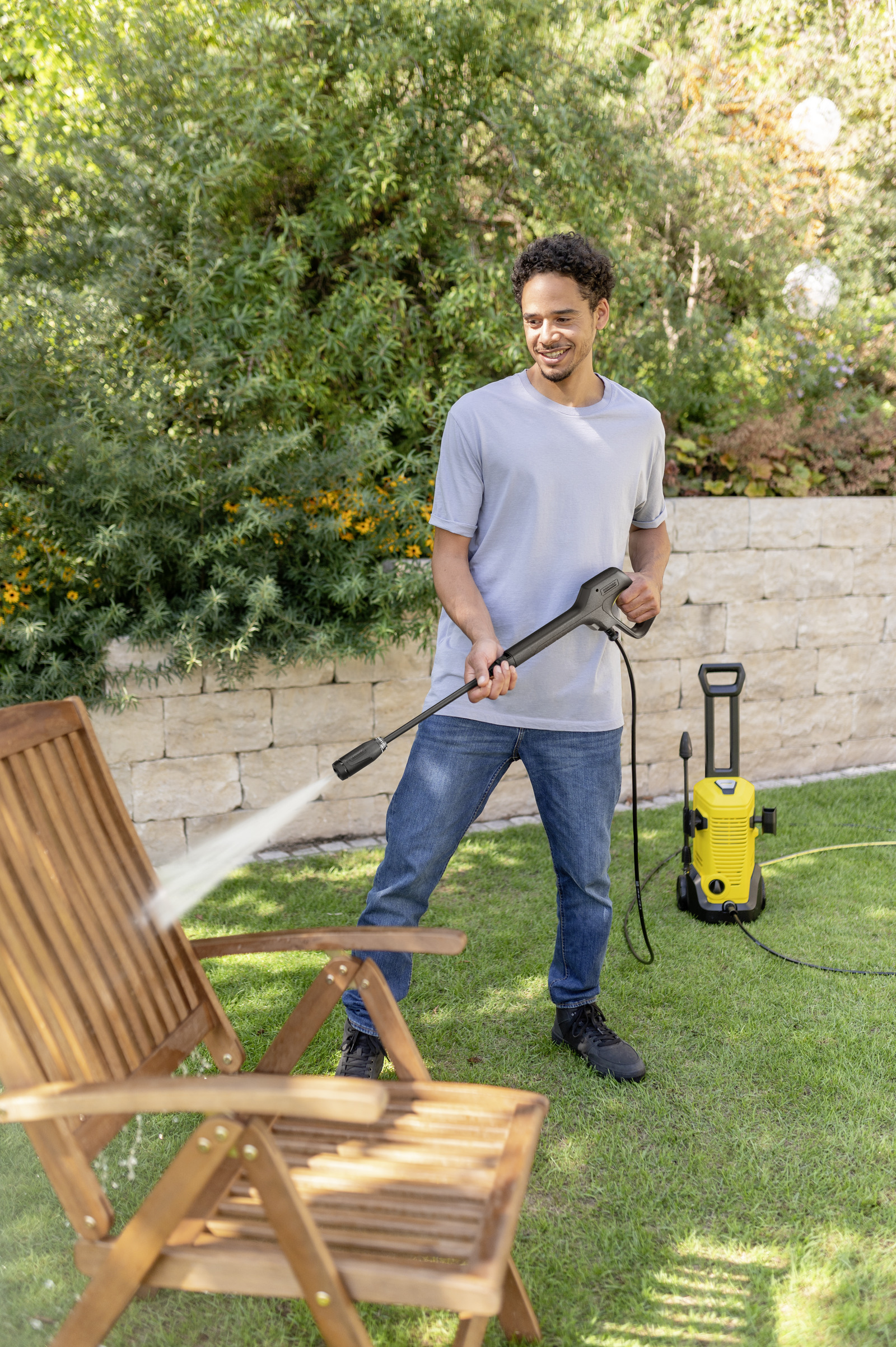 Un uomo pulisce una sedia di legno con un'idropulitrice in giardino.