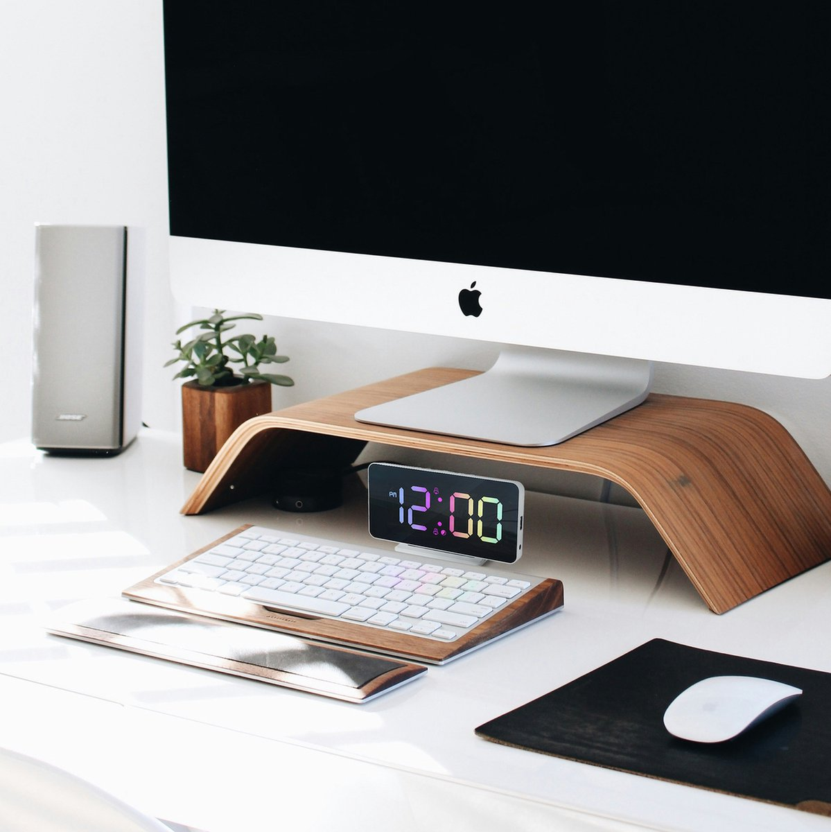 Ein Schreibtisch mit einem iMac, Tastatur, Maus und einem digitalen Wecker.