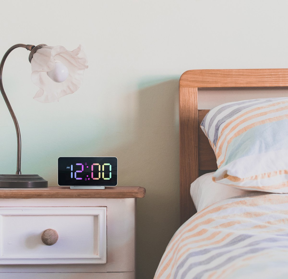 Ein digitaler Wecker zeigt 12:00 Uhr neben einem Nachttisch und einem Bett.