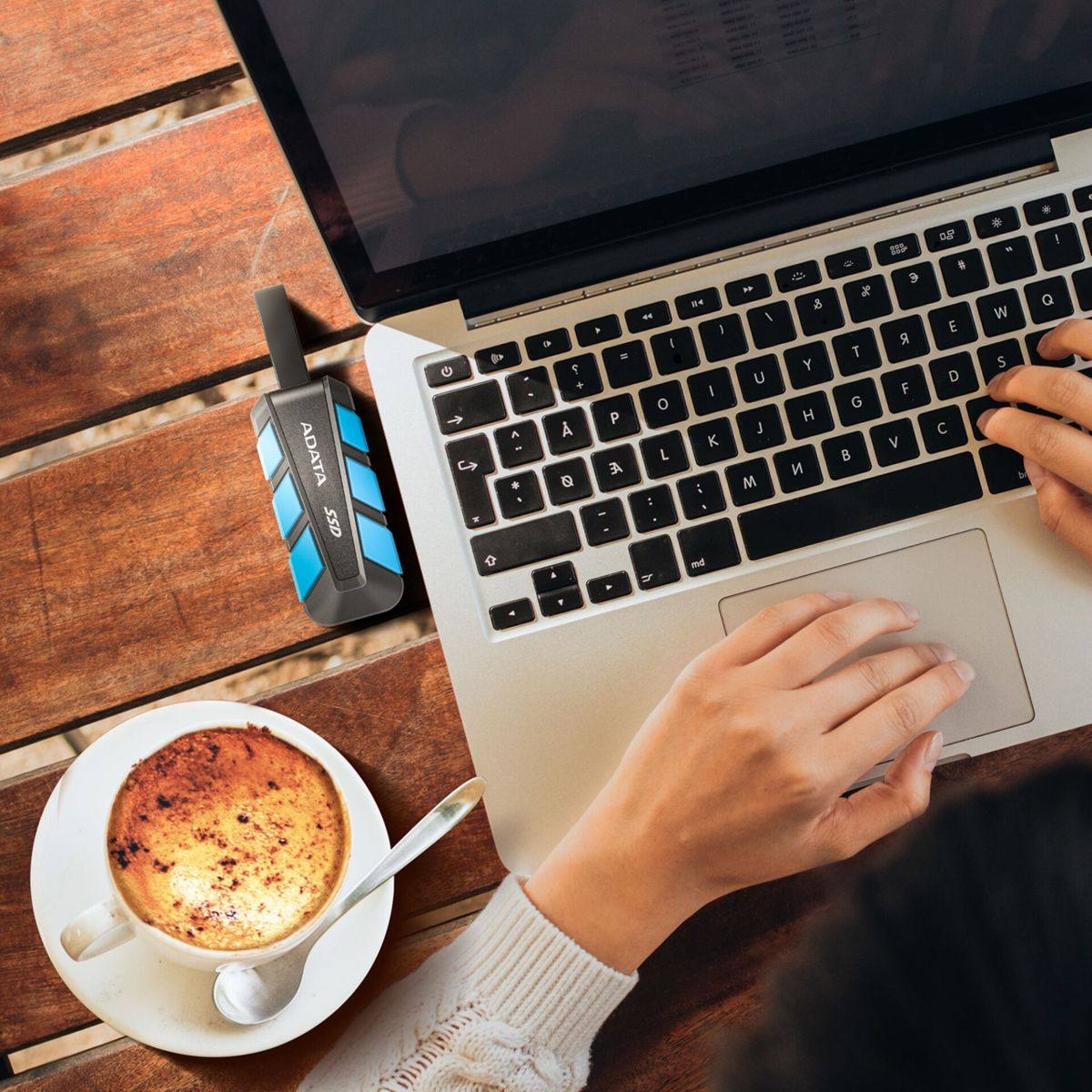 Ein Laptop, eine externe SSD und eine Kaffeetasse auf einem Holztisch.