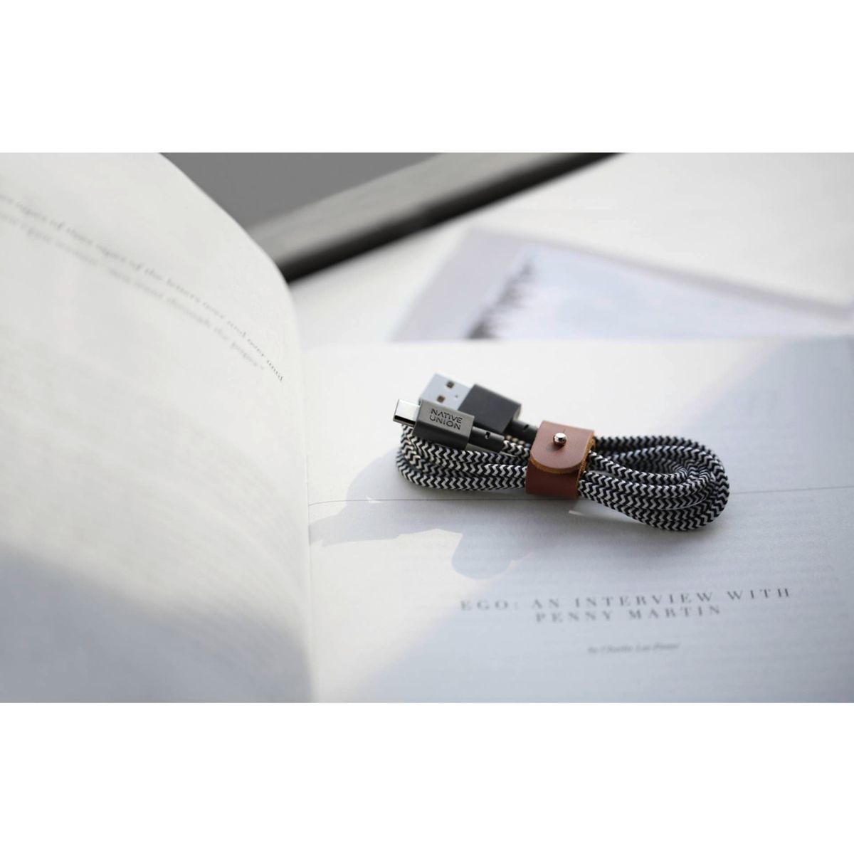 Ein schwarz-wei geflochtenes USB-Kabel mit braunem Lederriemen liegt auf einem Buch.