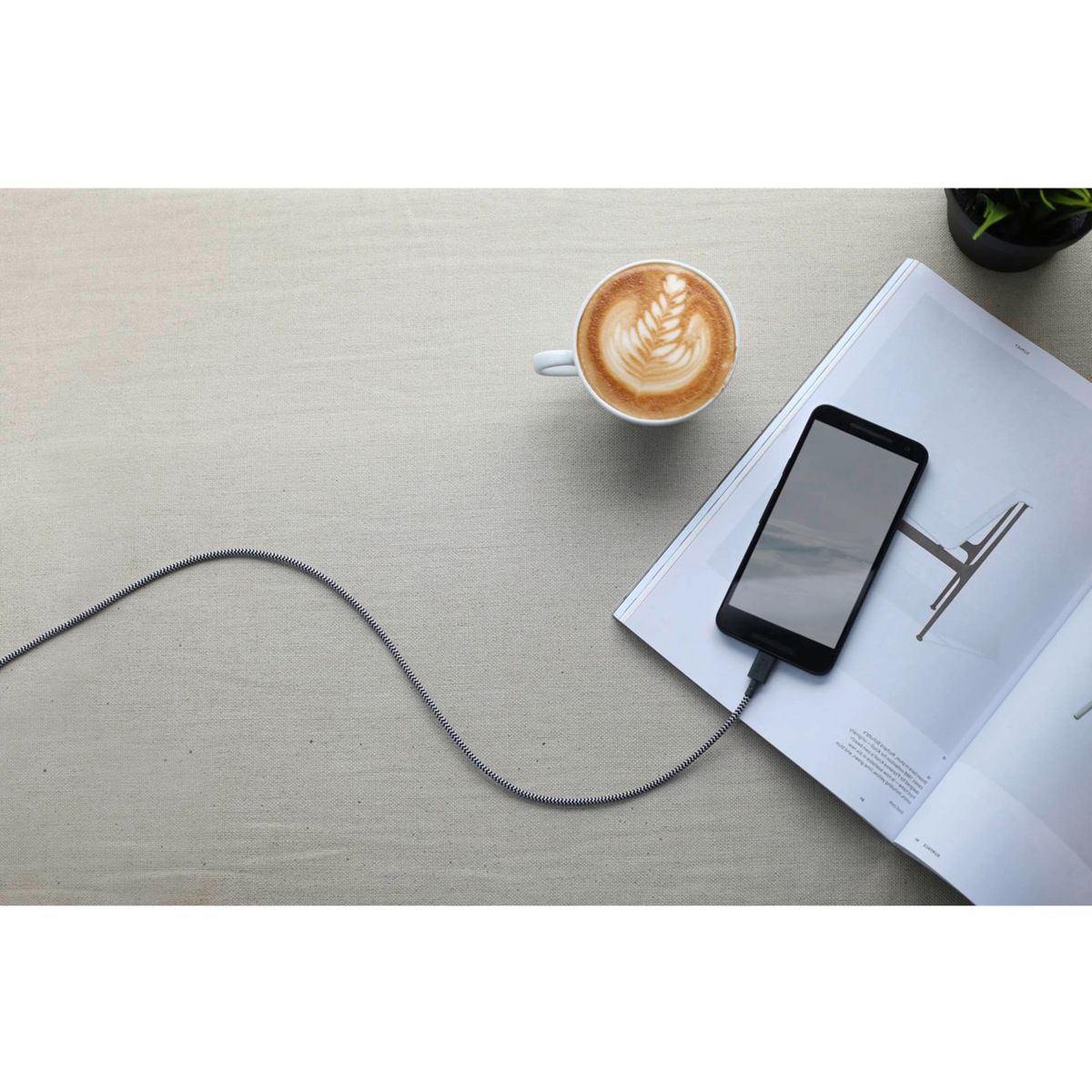 Tasse Kaffee neben Handy auf Magazin, Ladekabel angeschlossen.
