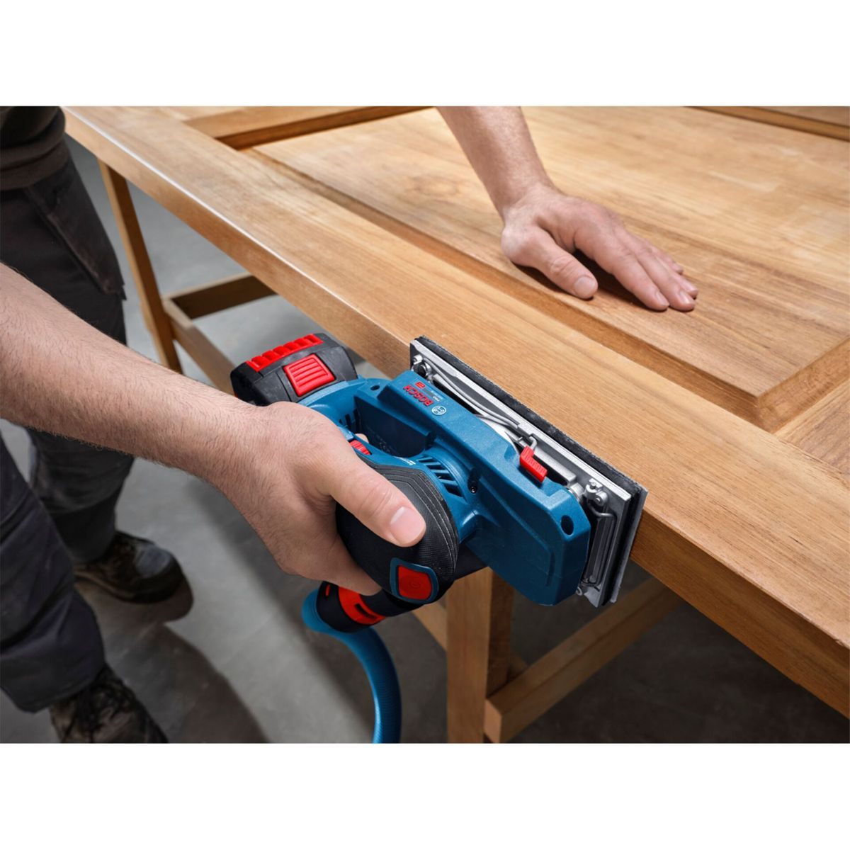 Mann schleift Holztür mit blauem Schleifgerät. Hände und Werkzeug sind im Fokus.