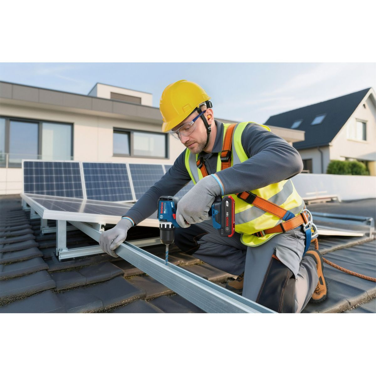 Ein Mann in Schutzkleidung bohrt auf einem Dach neben Solarmodulen.