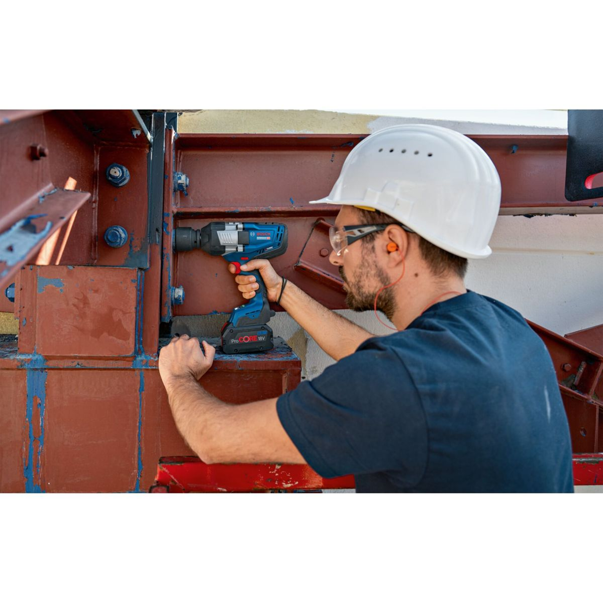 Mann mit Helm benutzt einen blauen Schlagschrauber an einer Metallkonstruktion.