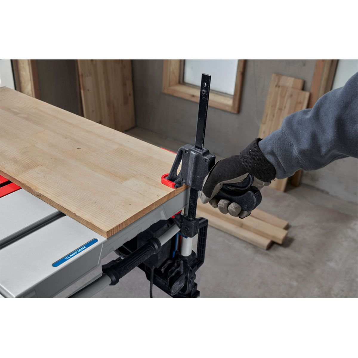 Person in Handschuhen klemmt Holzbrett an Werkbank mit Zwinge.