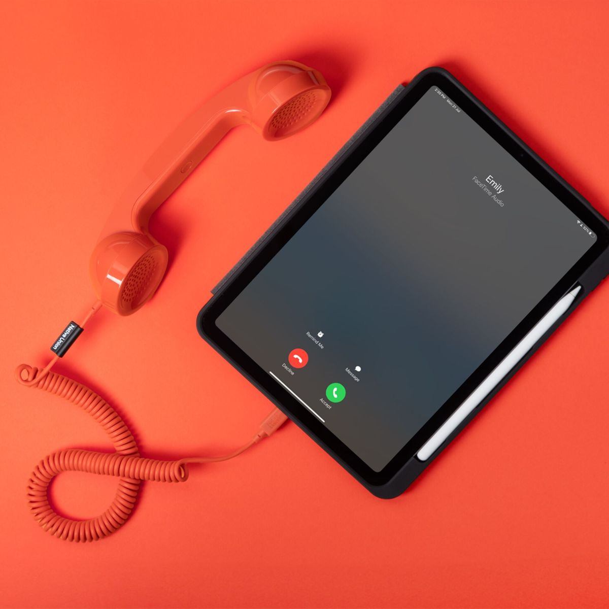 Un auricolare telefonico retrò arancione e un tablet con una chiamata in arrivo su sfondo rosso.