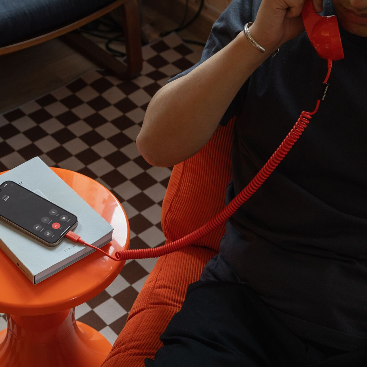Persona al telefono con una cornetta rossa collegata a uno smartphone.