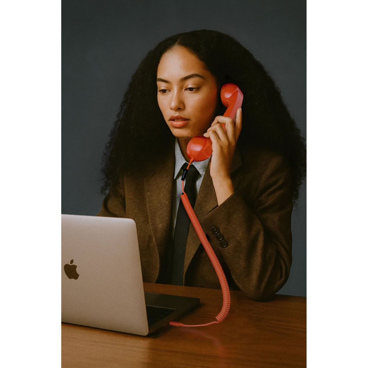 Una donna con lunghi capelli scuri parla al telefono rosso accanto a un laptop.