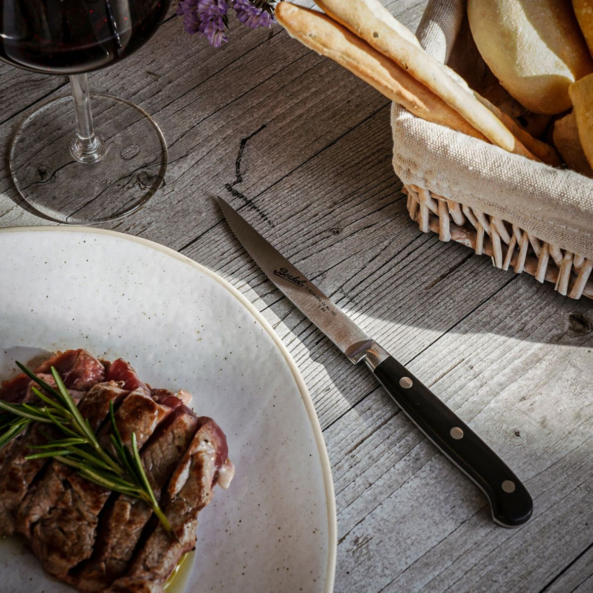 Ein Teller mit geschnittenem Steak, ein Weinglas und ein Brotkorb auf Holztisch.