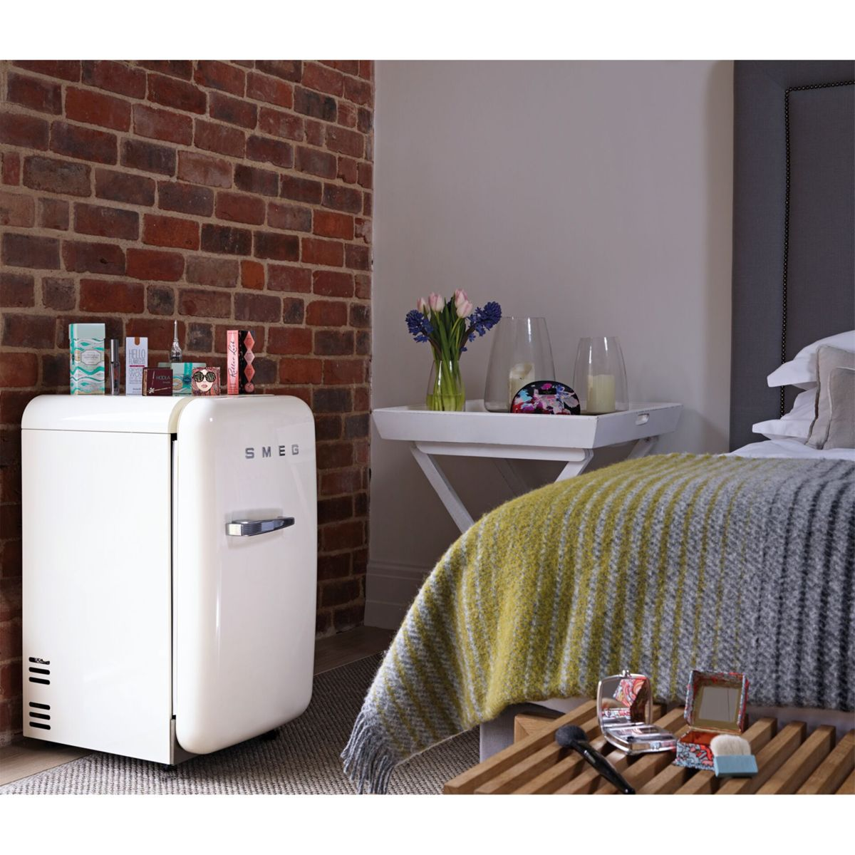 Ein weißer SMEG-Kühlschrank neben einem Bett mit einer Decke mit gelben und grauen Streifen.