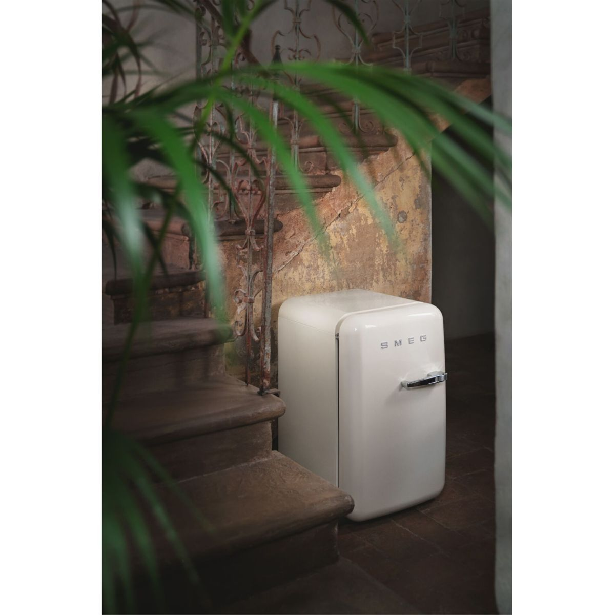 Ein cremefarbener Smeg-Kühlschrank steht neben einer alten Steintreppe mit einem schmiedeeisernen Geländer.