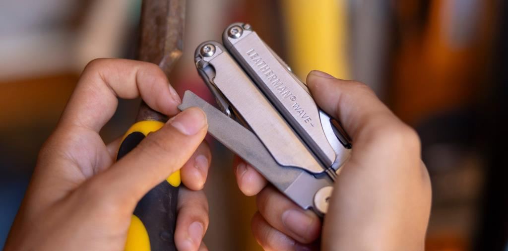 Bir el, sarı saplı bir nesneyi törpülemek için Leatherman Wave+ çok amaçlı alet kullanıyor.