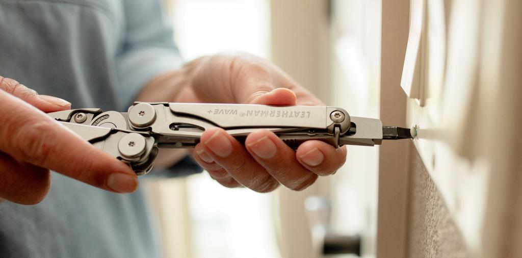 Bir kişi beyaz bir yüzeye vida takmak için Leatherman çok amaçlı alet kullanıyor.