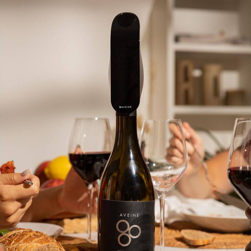 Un aeratore per vino Aveine è attaccato a una bottiglia di vino, circondato da bicchieri e cibo.