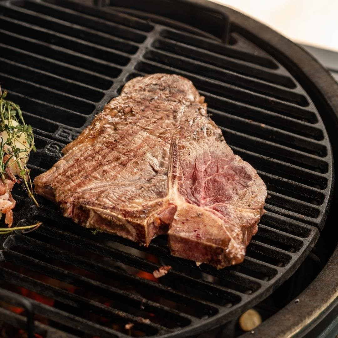 T-bone biftek, yanında otlarla birlikte sıcak közlerin üzerinde ızgara ızgarasında pişiyor.