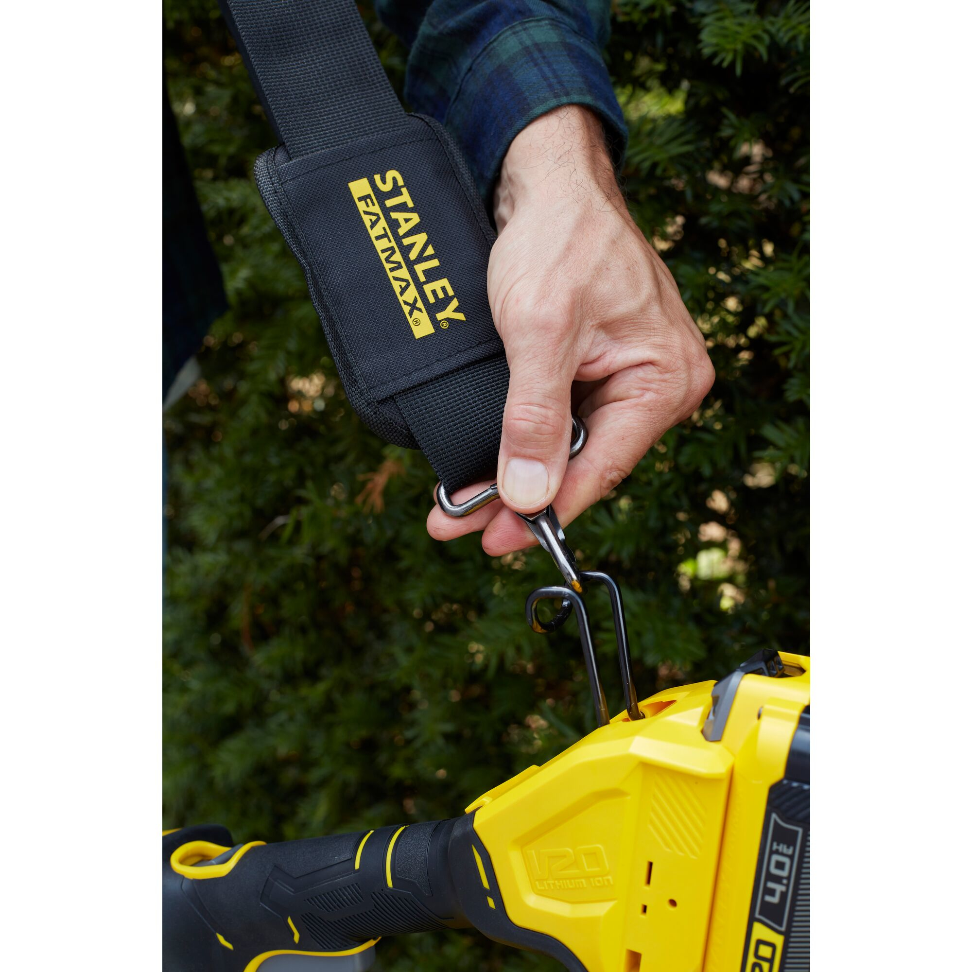 Una mano aggancia una cinghia Stanley FatMax a un attrezzo elettrico giallo con batteria.