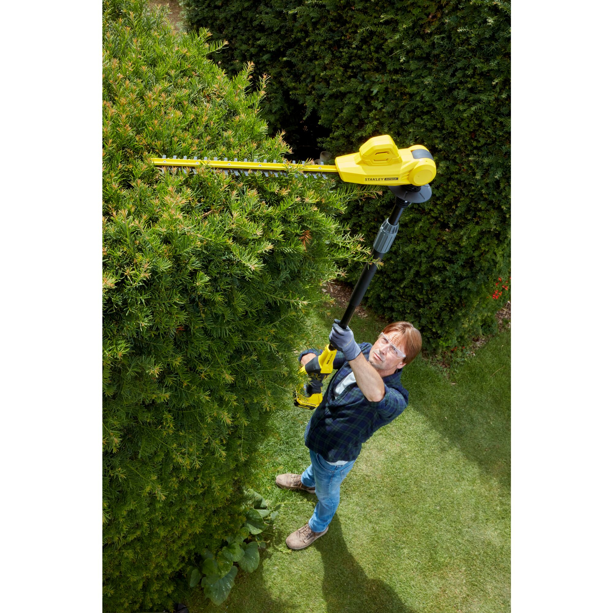 Uomo pota siepe con tagliasiepi giallo in giardino.