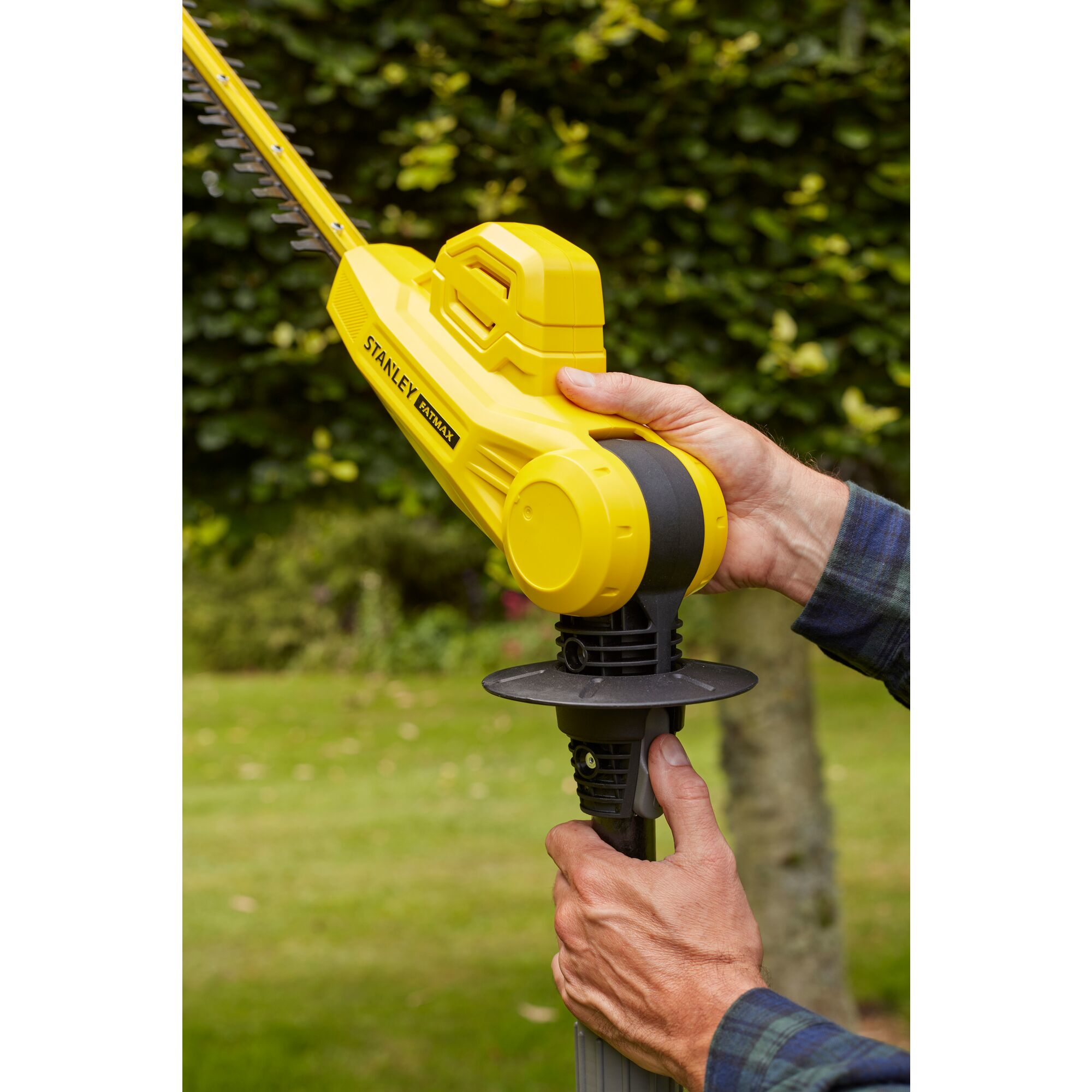Tagliasiepi giallo tenuto in mano, sfondo di fogliame verde.