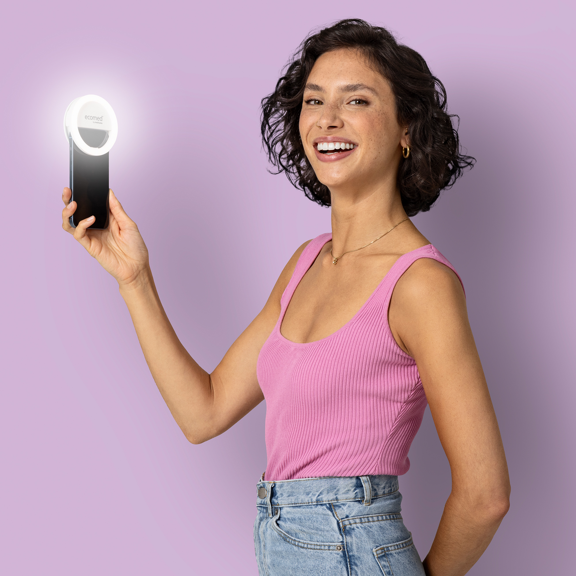 Una mujer de pelo oscuro sostiene un smartphone con un aro de luz delante.