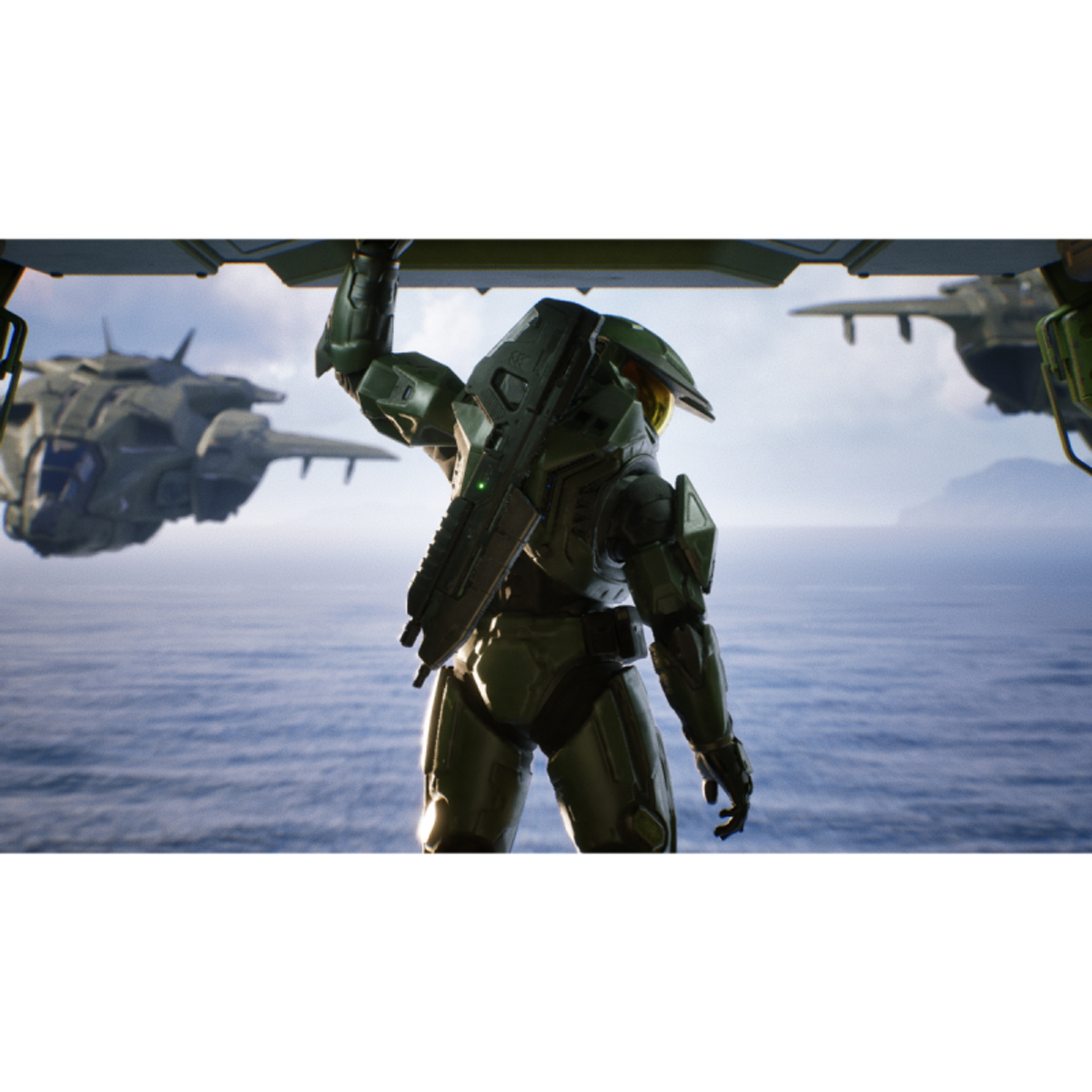 Master Chief sostiene un arma, mirando al mar con una nave de desembarco al fondo.
