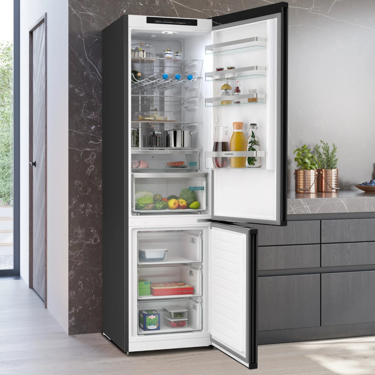 Un refrigerador negro abierto con alimentos, incluyendo frutas, verduras y botellas.