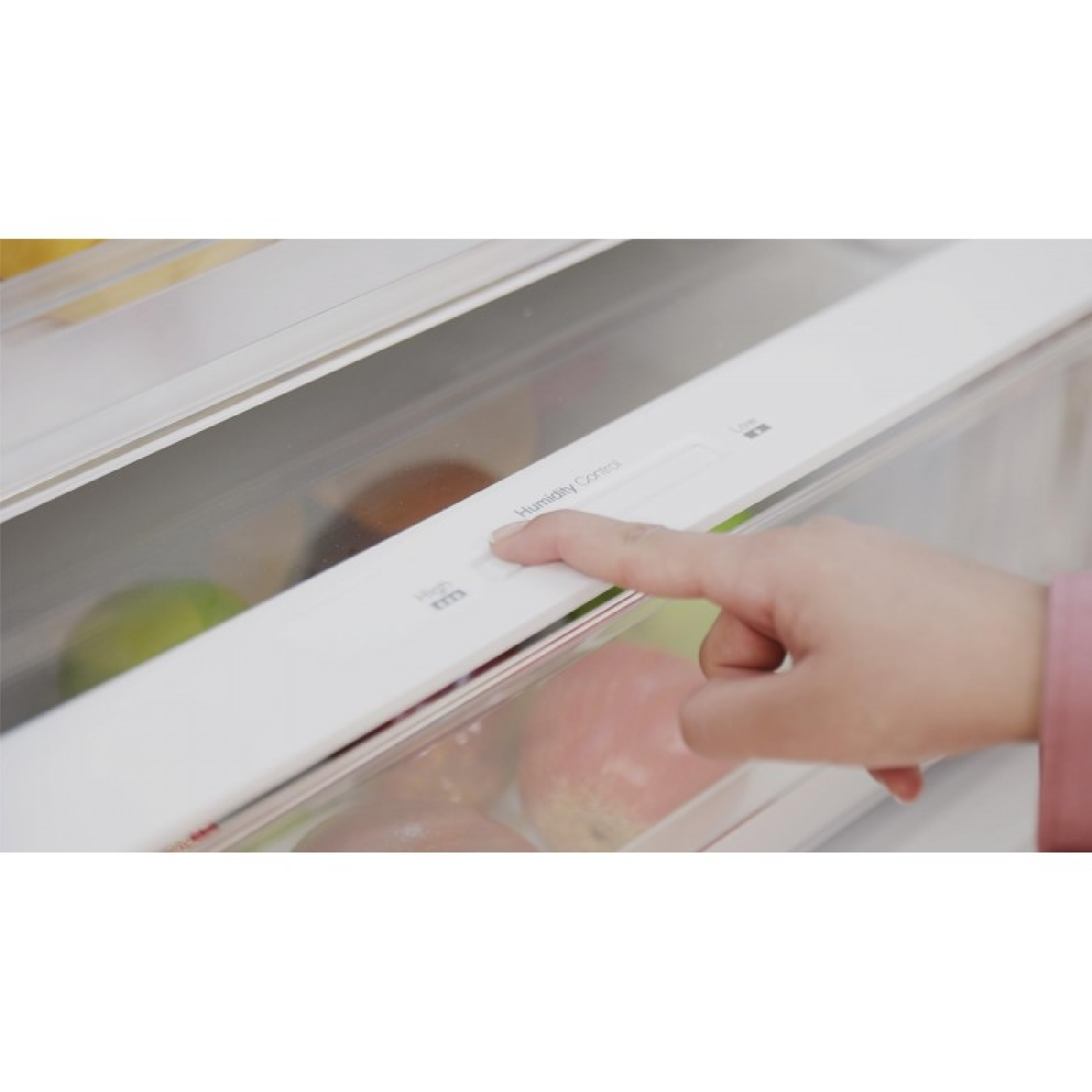 Una mano ajusta el control de humedad en un cajón del refrigerador lleno de manzanas y limas.