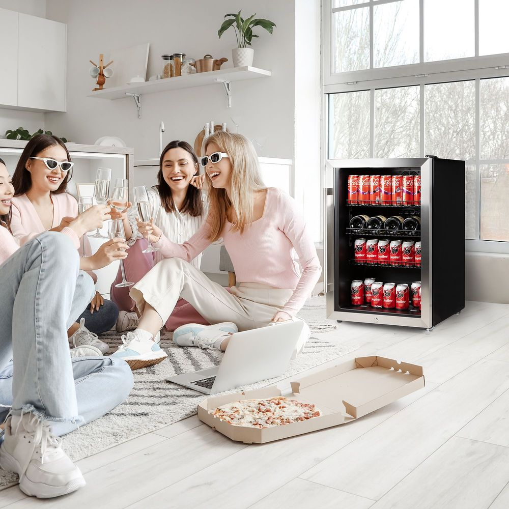 Quattro donne brindano con champagne, con pizza e minifrigo nelle vicinanze.