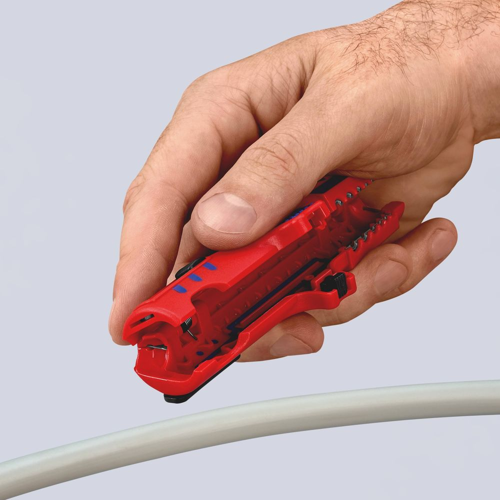 Una mano tiene una spelafili rossa sopra un cavo grigio, pronta a spellarlo. L'utensile ha accenti neri e blu.