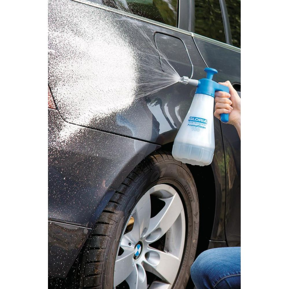 Spruzzatore a schiuma spruzza schiuma su un'auto scura vicino alla ruota.
