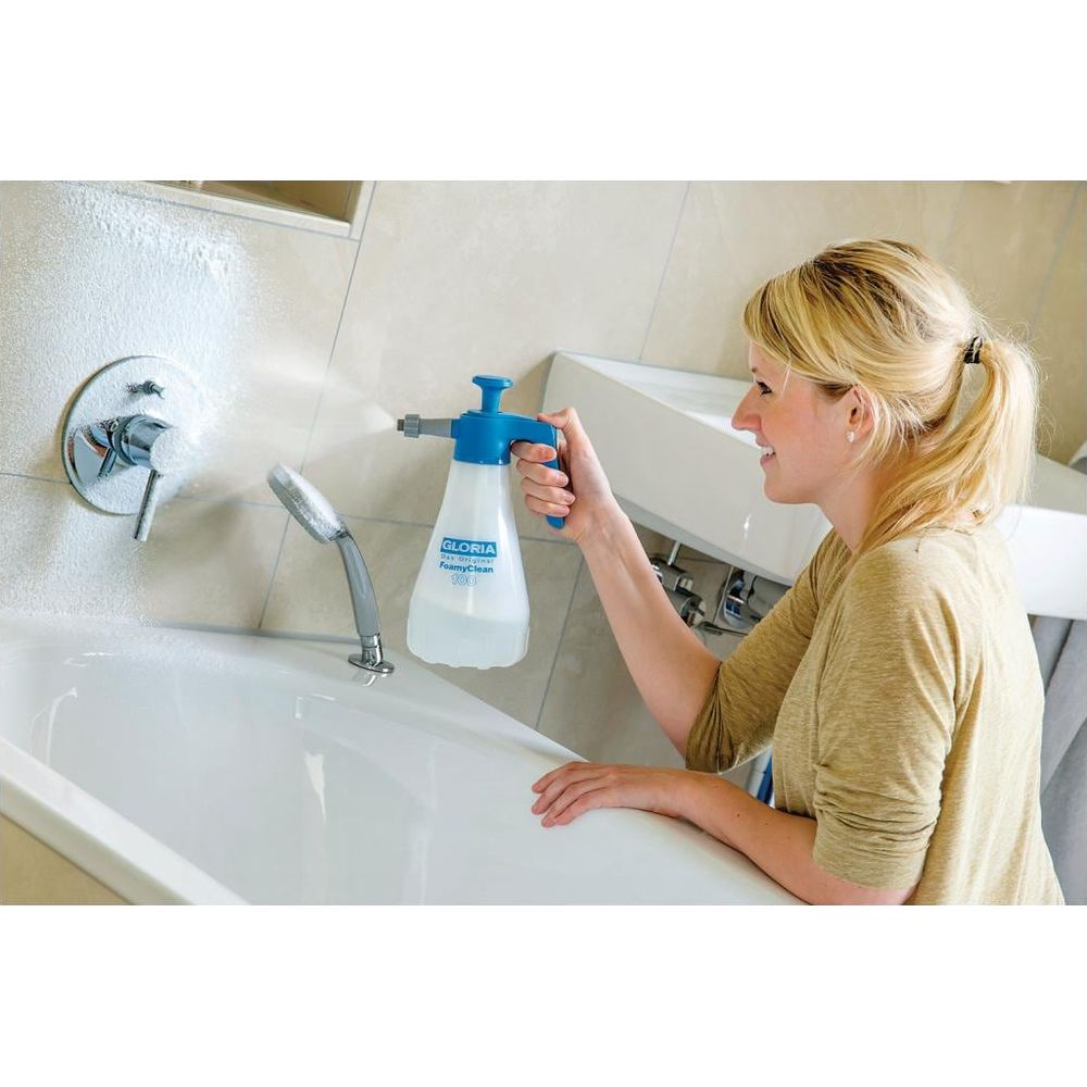 Una donna spruzza schiuma in una vasca da bagno bianca con uno spruzzatore blu.