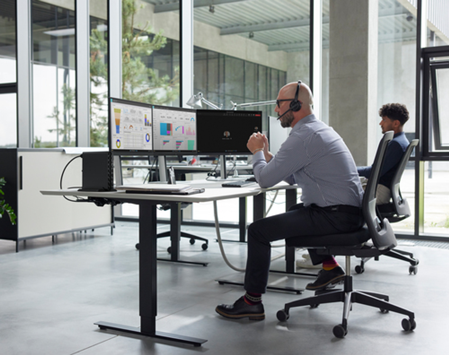 Due uomini lavorano ai computer in un ufficio moderno. Uno indossa un auricolare.