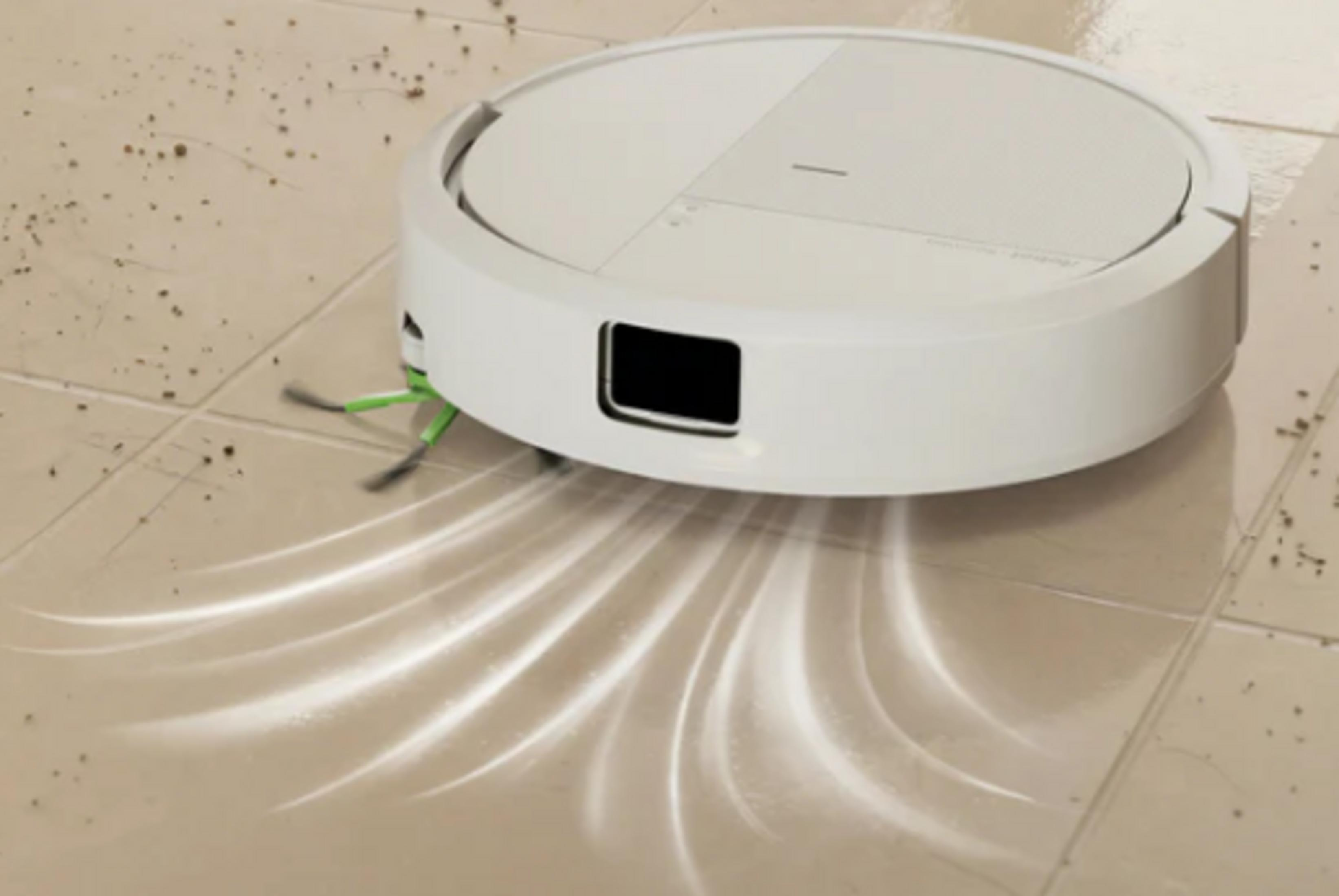Un robot aspirapolvere bianco pulisce un pavimento piastrellato chiaro, raccogliendo detriti.