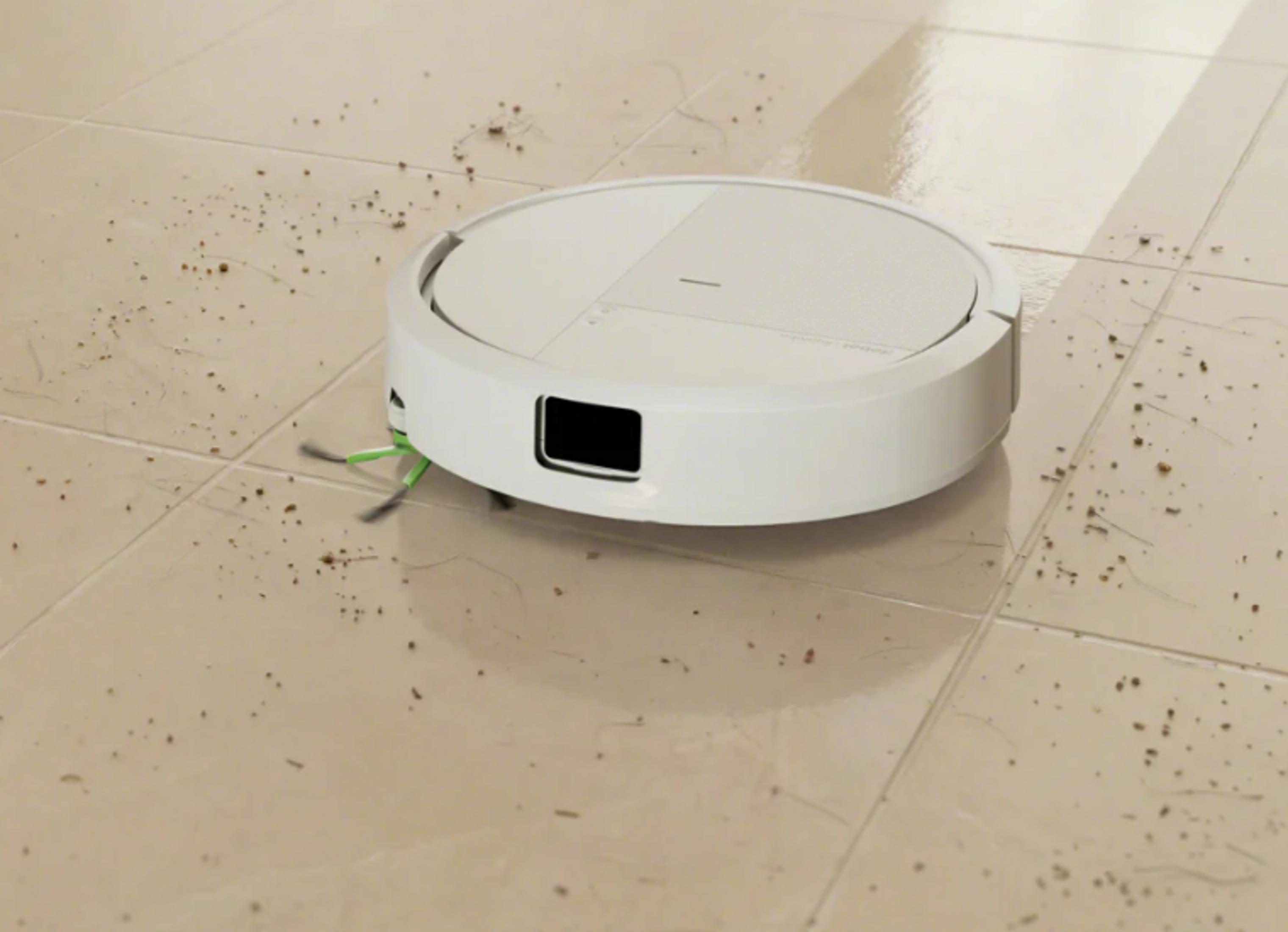 Un robot aspirapolvere bianco pulisce un pavimento piastrellato sporco.