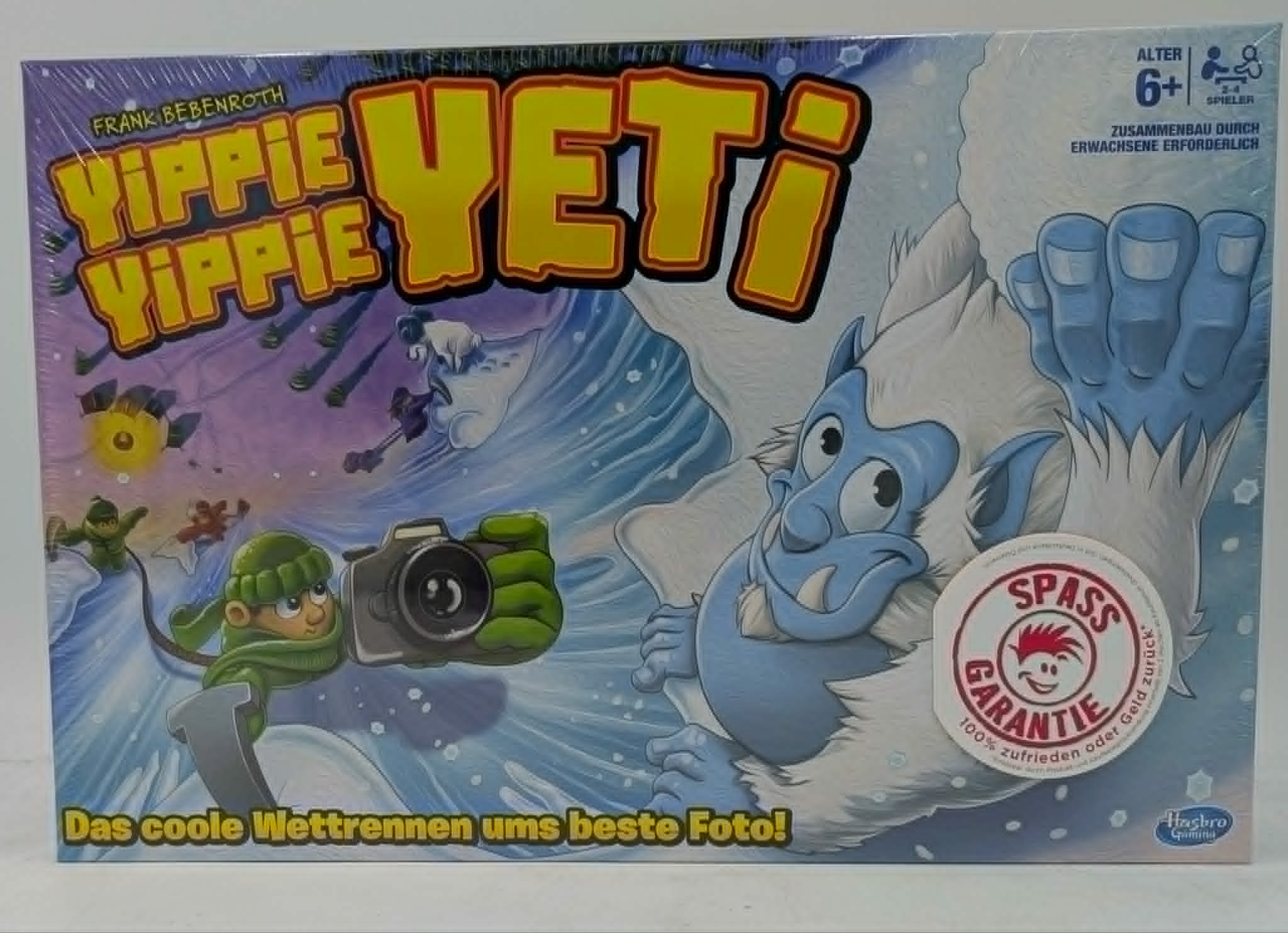 Brettspiel-Cover: Ein Yeti und Kinder im Schnee, die ein Foto machen.