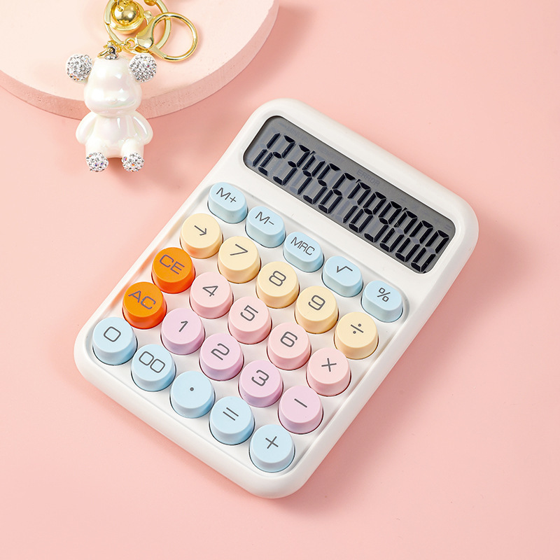 Ein weißer Taschenrechner mit bunten runden Tasten und einer Digitalanzeige mit '123456789000' liegt auf einer rosafarbenen Oberfläche neben einem weißen Bärenschlüsselanhänger.