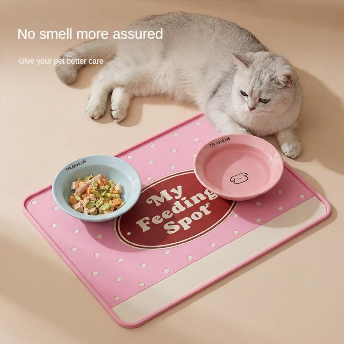 Eine graue Katze liegt auf einer rosa Futtermatte mit zwei Schalen, eine mit Futter, eine mit Wasser.