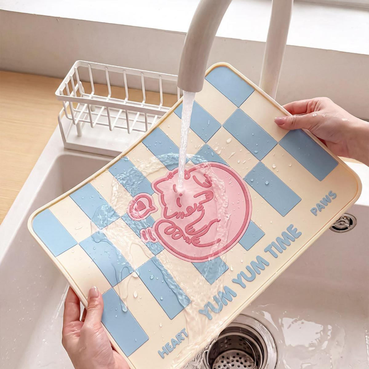 Hände waschen eine beige-blaue karierte Geschirrtrockenmatte mit rosa Katzenmotiv unter fließendem Wasser in einem Waschbecken.