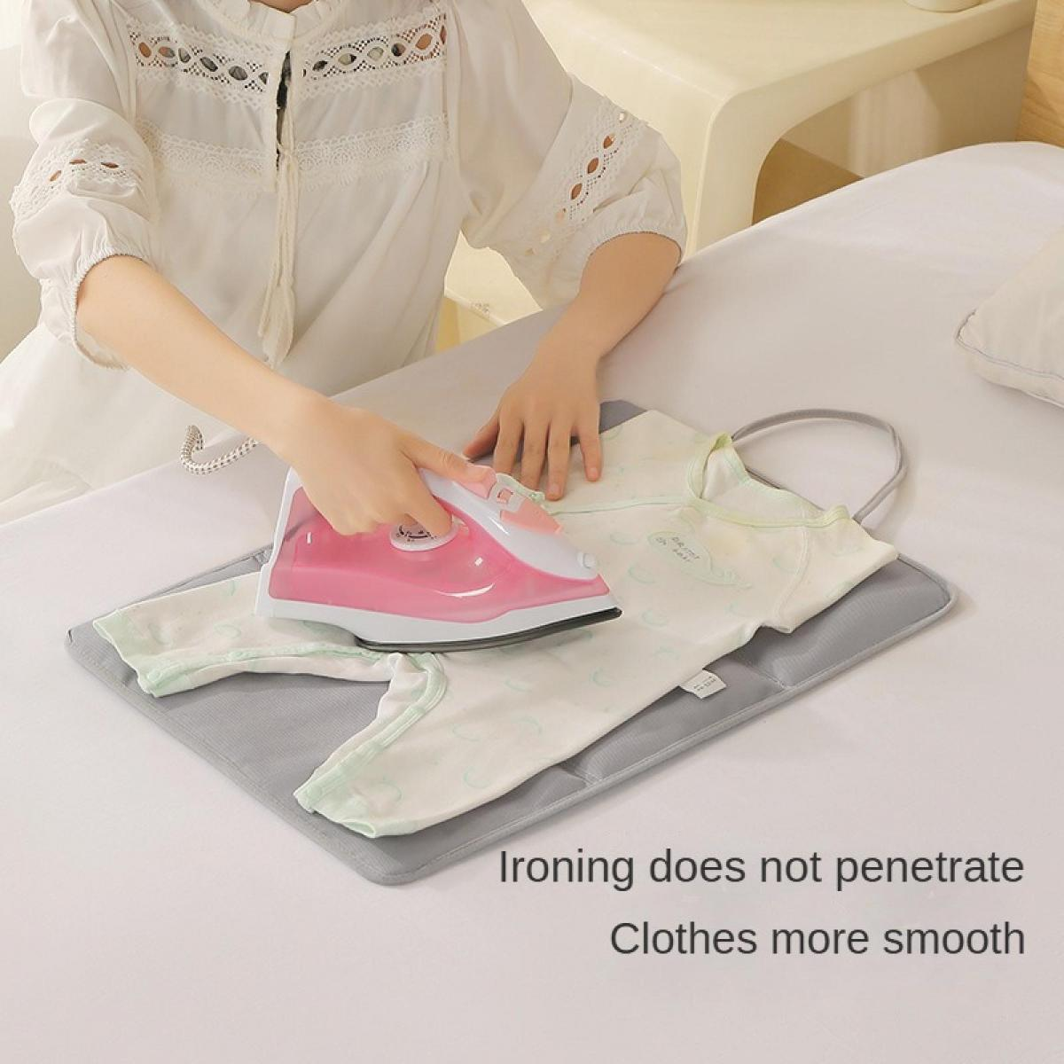 Eine Person bügelt ein Babyoutfit auf einer tragbaren Bügelmatte auf einem Bett.