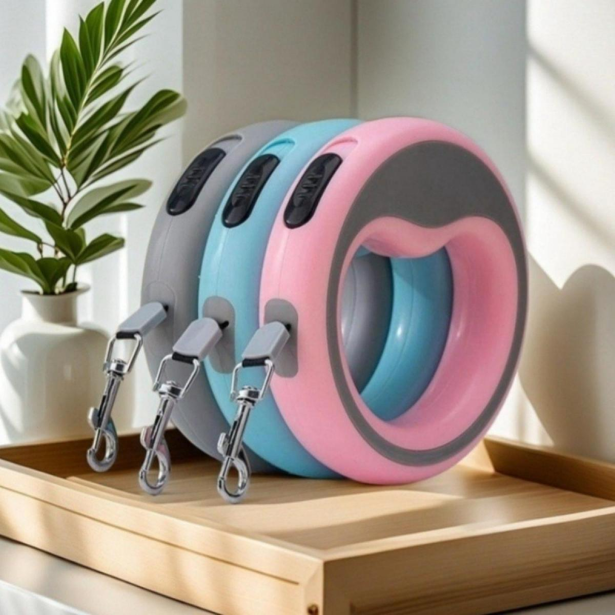 Drei Roll-Hundeleinen in Pink, Blau und Grau mit Metallclips liegen auf einem Holztablett.
