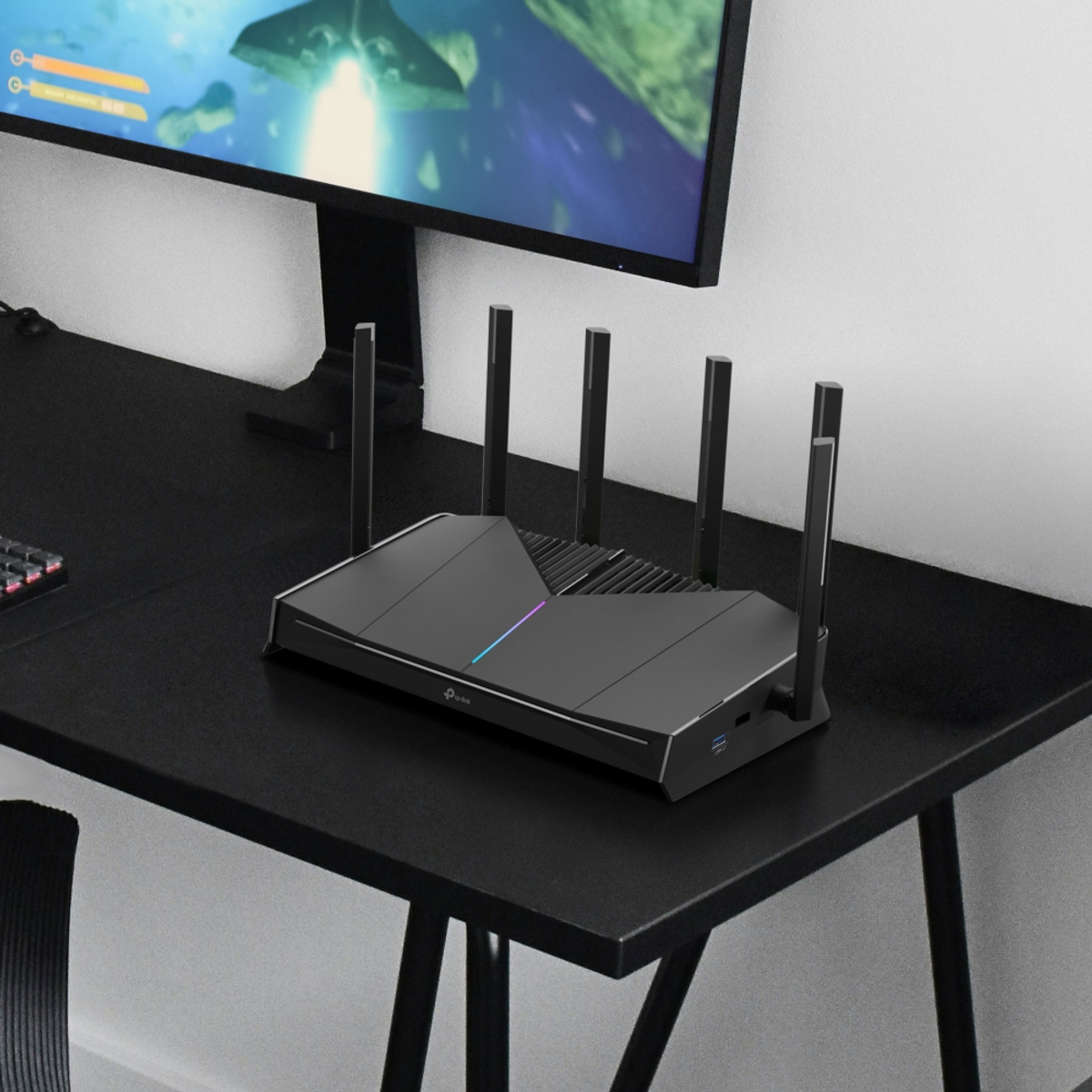 Un router nero con antenne è su una scrivania nera accanto a un monitor.