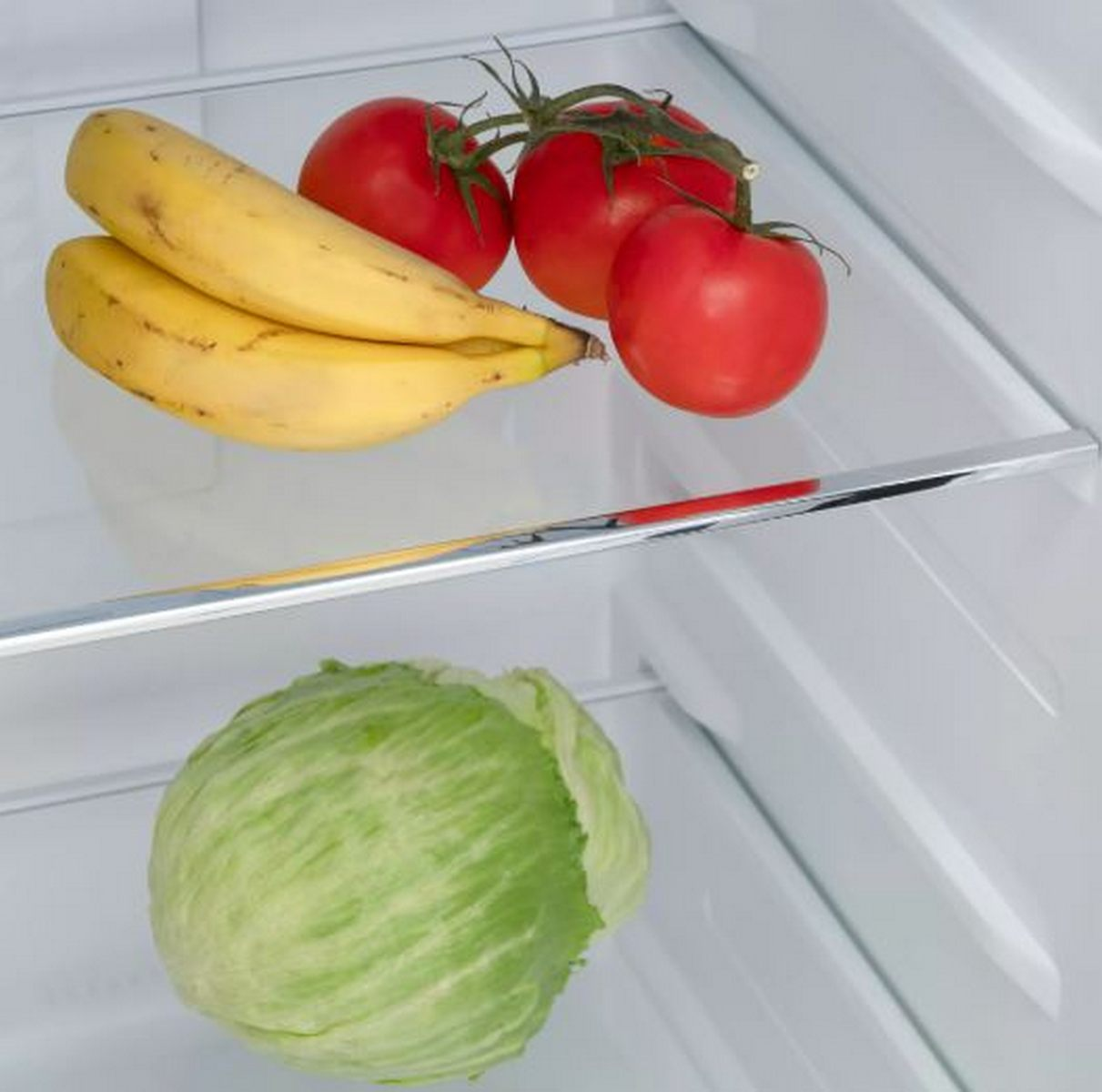 Plátanos y tomates en un estante de refrigerador sobre una lechuga.